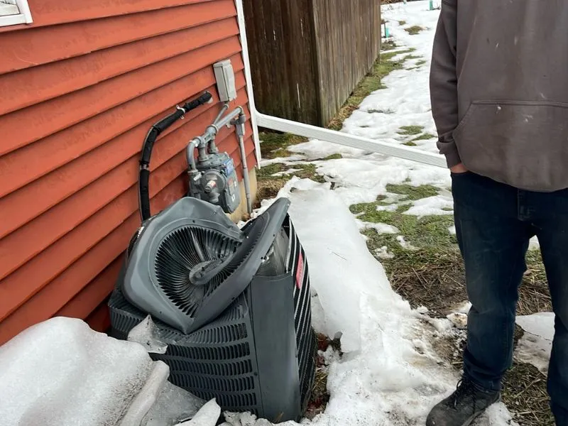 Winter gutter and ice damage to an outdoor air conditioning unit beside a Hamburg NY home