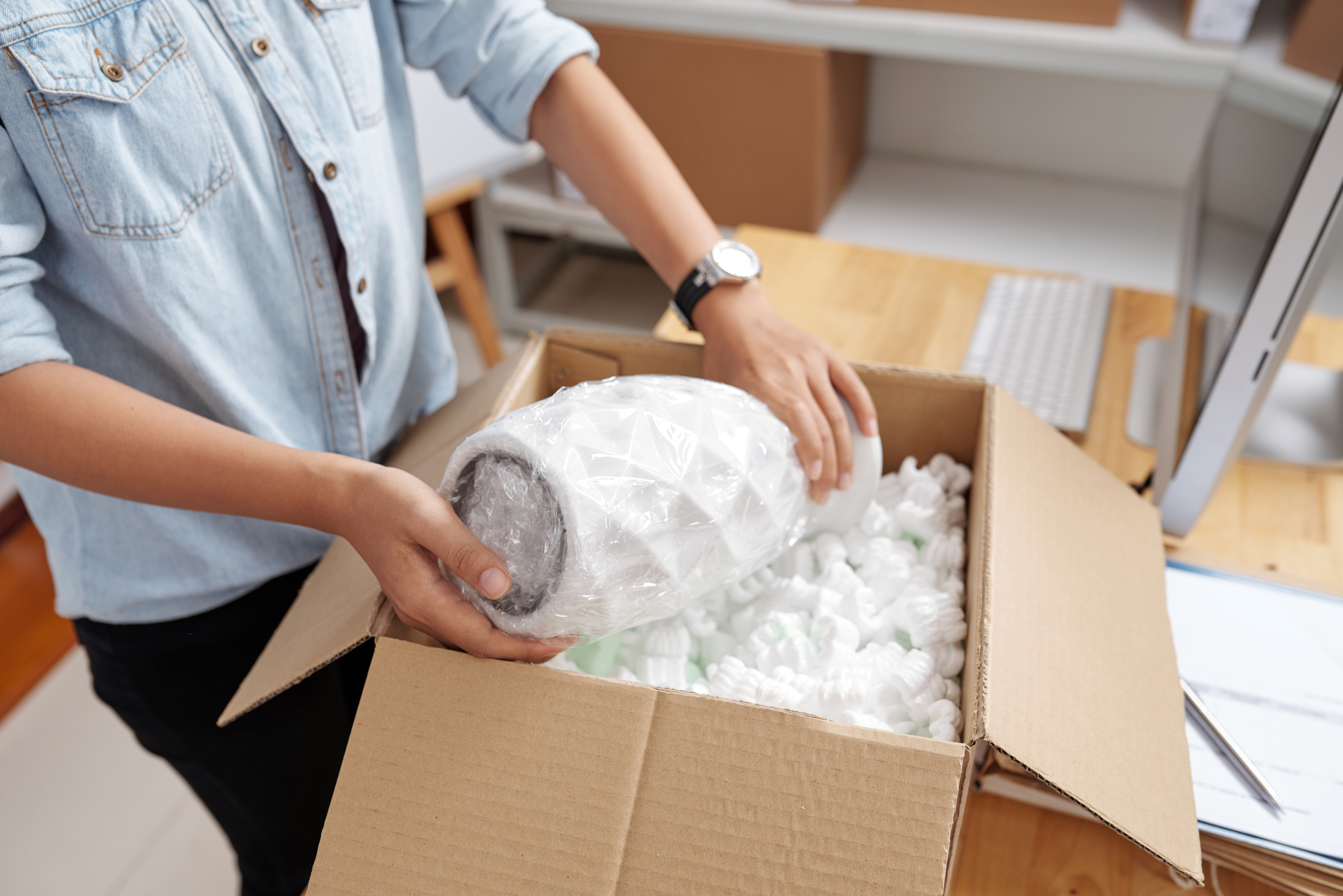 Person packing a fragile item with bubble wrap and packing peanuts in a shipping box, demonstrating professional packing for safe and secure delivery