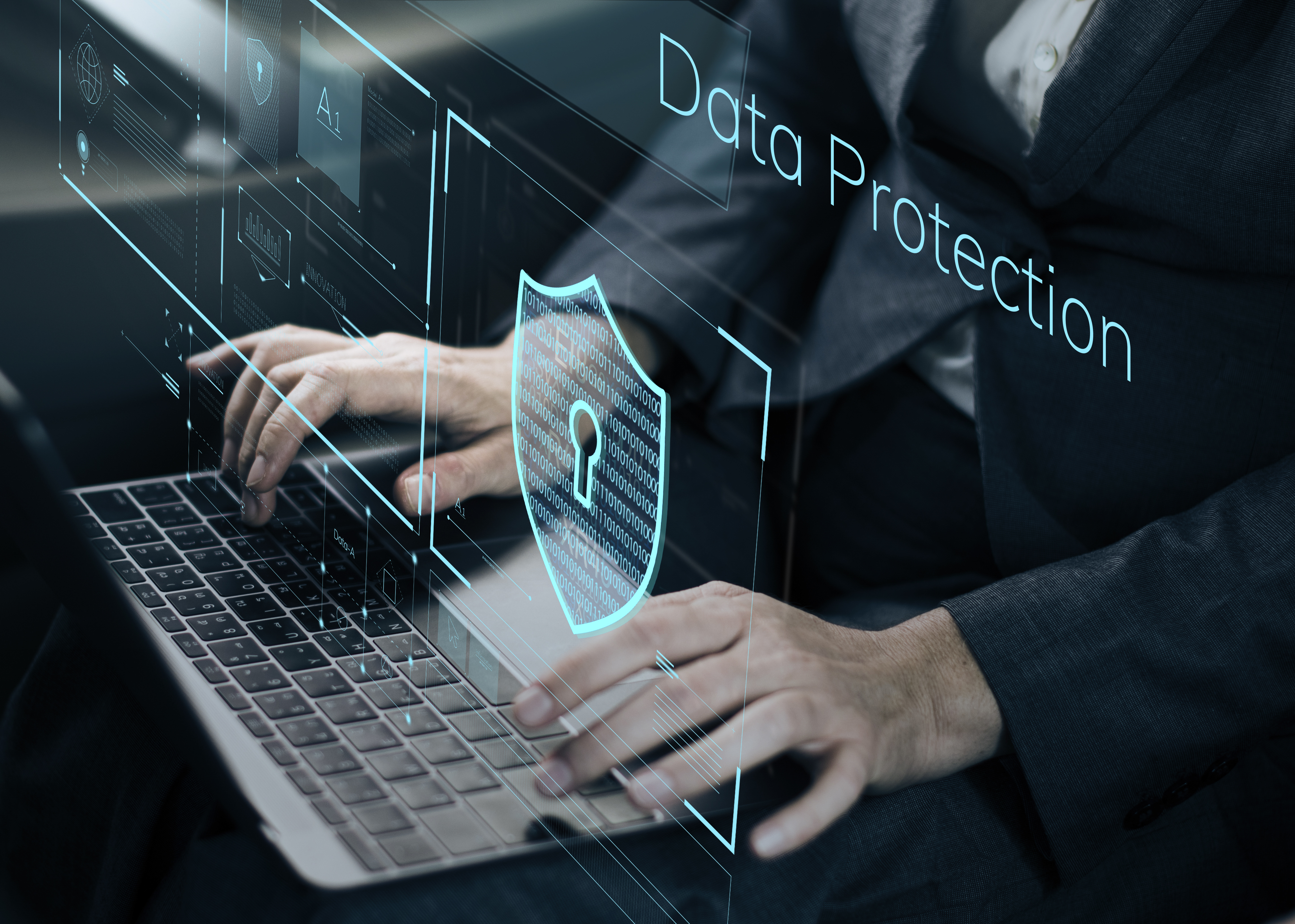 Business professional working on a laptop with digital data protection and cybersecurity graphics displayed on screen, representing business security, data privacy, information protection, cyber risk management, and secure business operations.