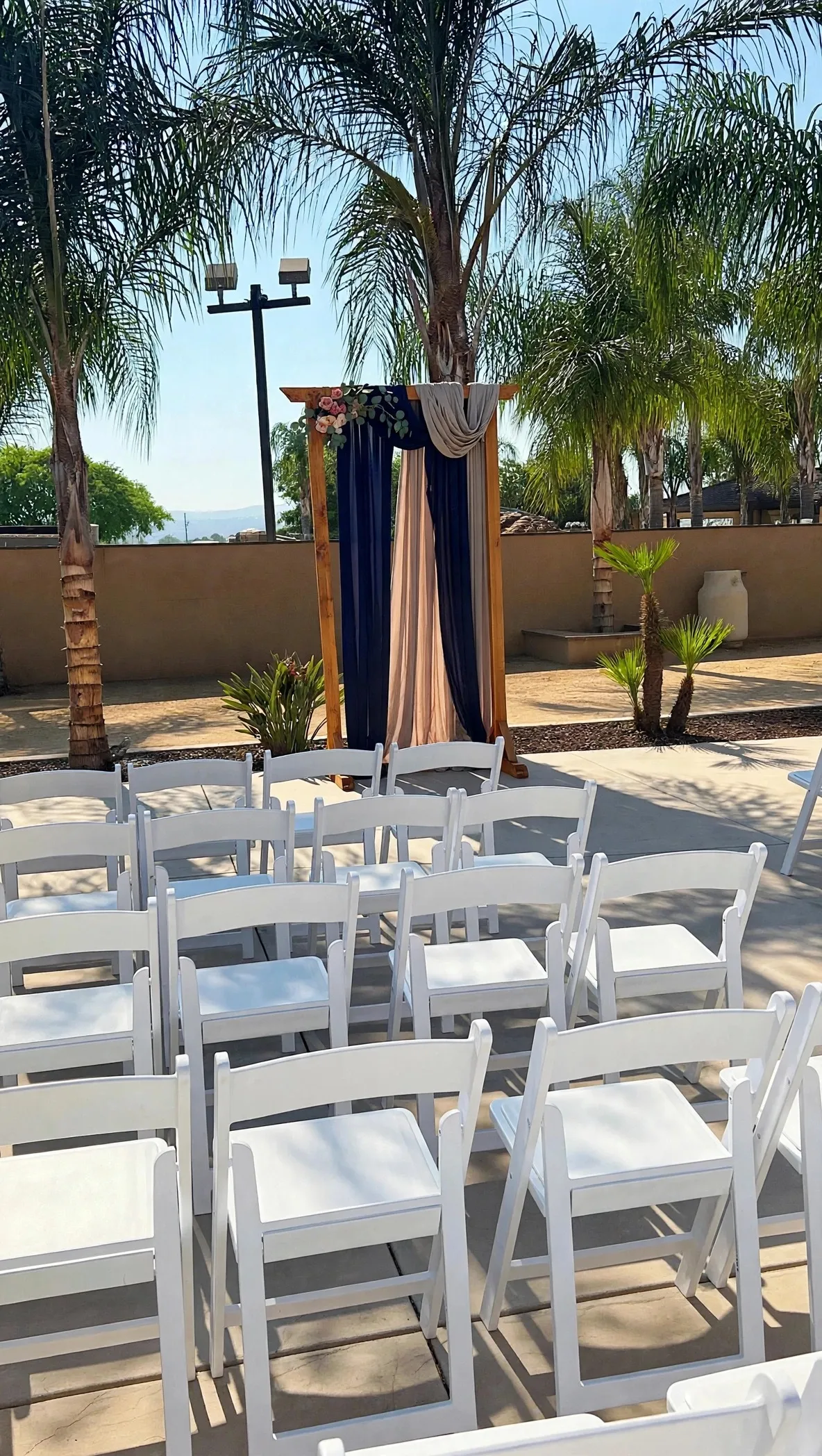 Sunlit outdoor wedding reception table set with ivory linens, earthen ceramics, and olive sprigs
