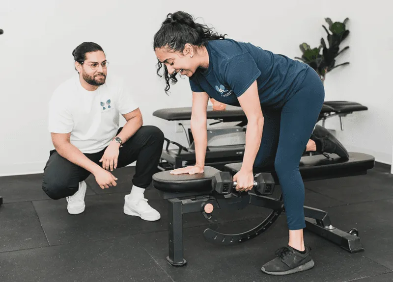 A patient performing dumbbell press on a bench & the trainer looking at her in Vancouver, Surrey & Langley