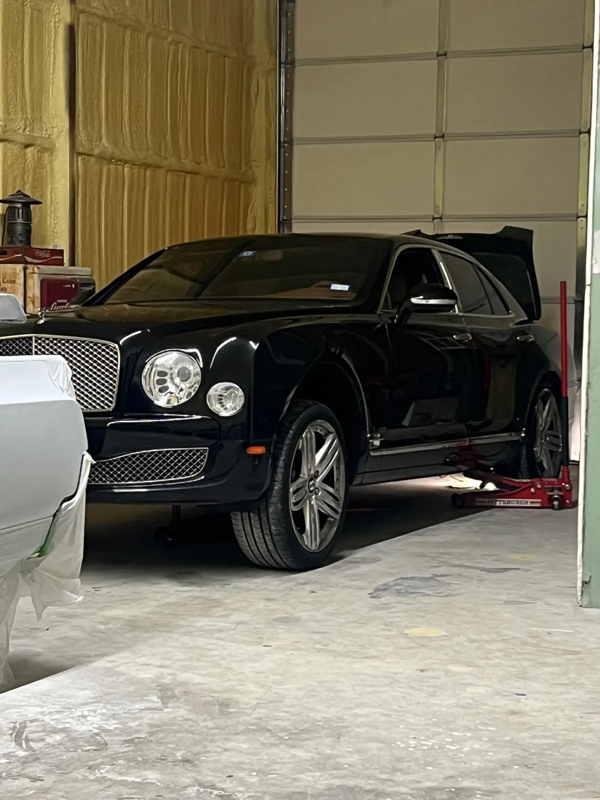 Black luxury vehicle, a Bentley, in an automotive garage with a raised jack, showcasing Kanewske Motors' restoration and service capabilities.