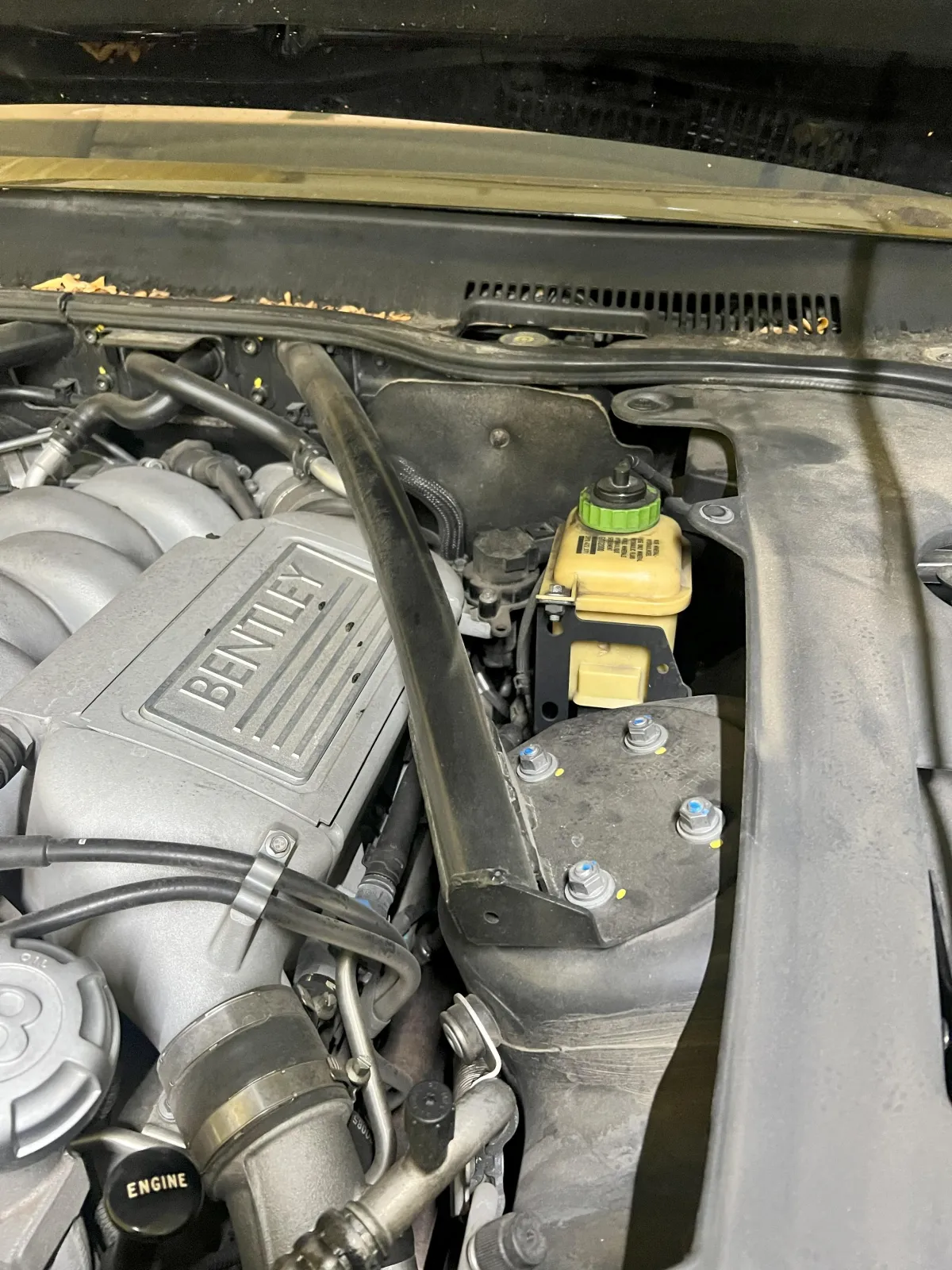 Engine compartment of a Bentley vehicle showcasing detailed components, including the engine cover and fluid reservoir, highlighting the quality of automotive service at Kanewske Motors.