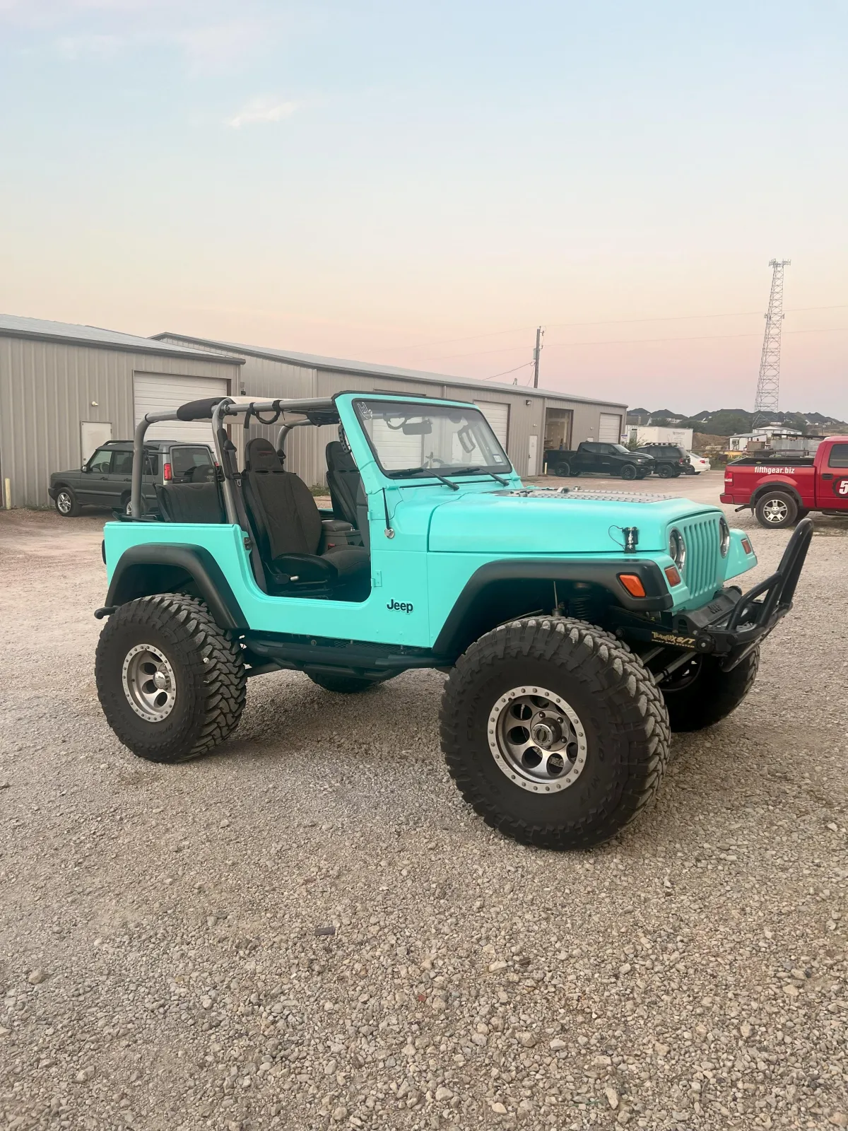 Jeep Wrangler in vibrant turquoise color parked on gravel, showcasing custom modifications and off-road tires, highlighting Kanewske Motors' automotive restoration services.
