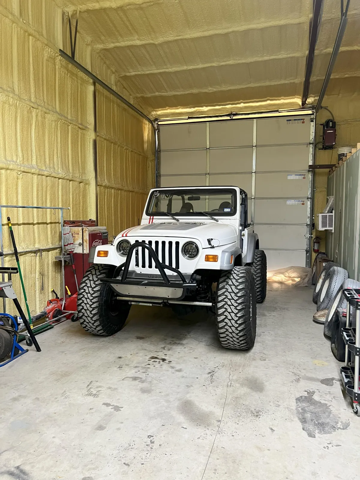 White Jeep Wrangler parked inside a garage with insulated walls, showcasing Kanewske Motors' automotive restoration and service capabilities.