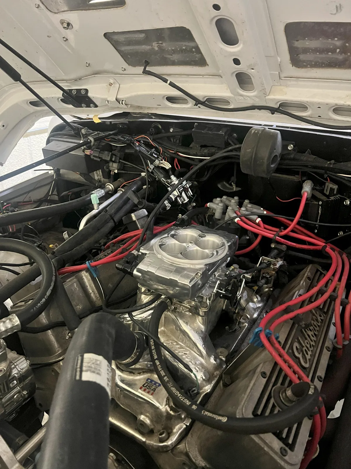 Engine compartment showcasing a detailed view of automotive components, including an Edelbrock intake manifold and red ignition wires, highlighting Kanewske Motors' automotive service and restoration expertise.