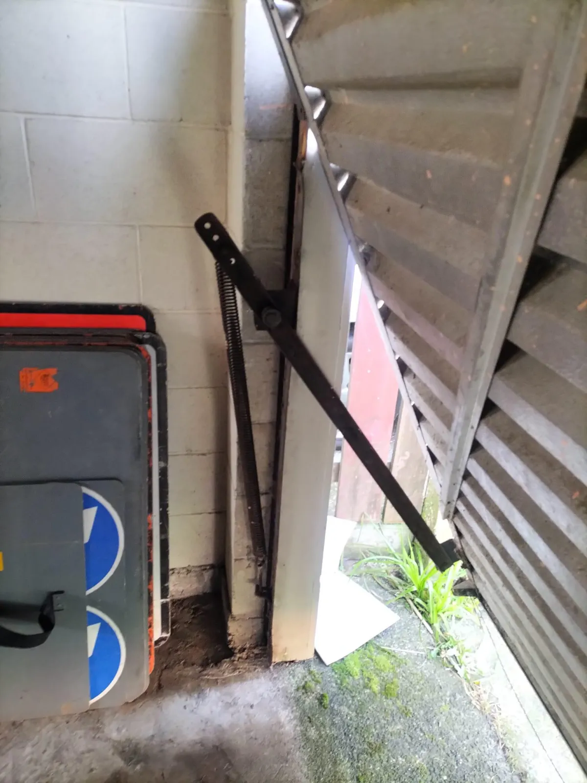 Interior shot of a damaged or misaligned tilt-style garage door showing the spring mechanism and exposed floor area.