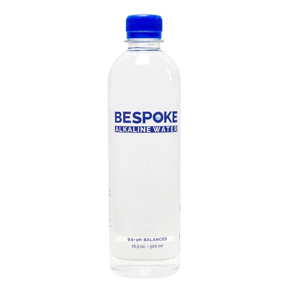 A plastic bottle of 9.5+ PH balanced Alkaline water made by HH Bespoke is placed on a table, and water droplets on the bottle indicate a refreshing quality.