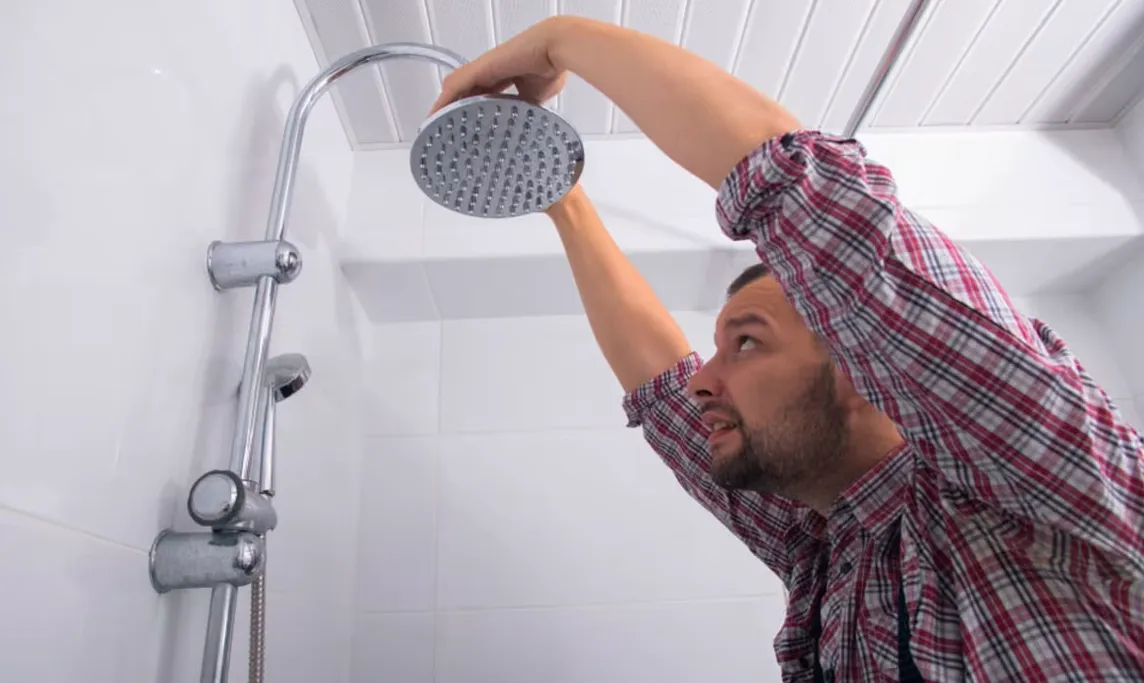 Technician installing a shower head in a nearly completed shower remodel