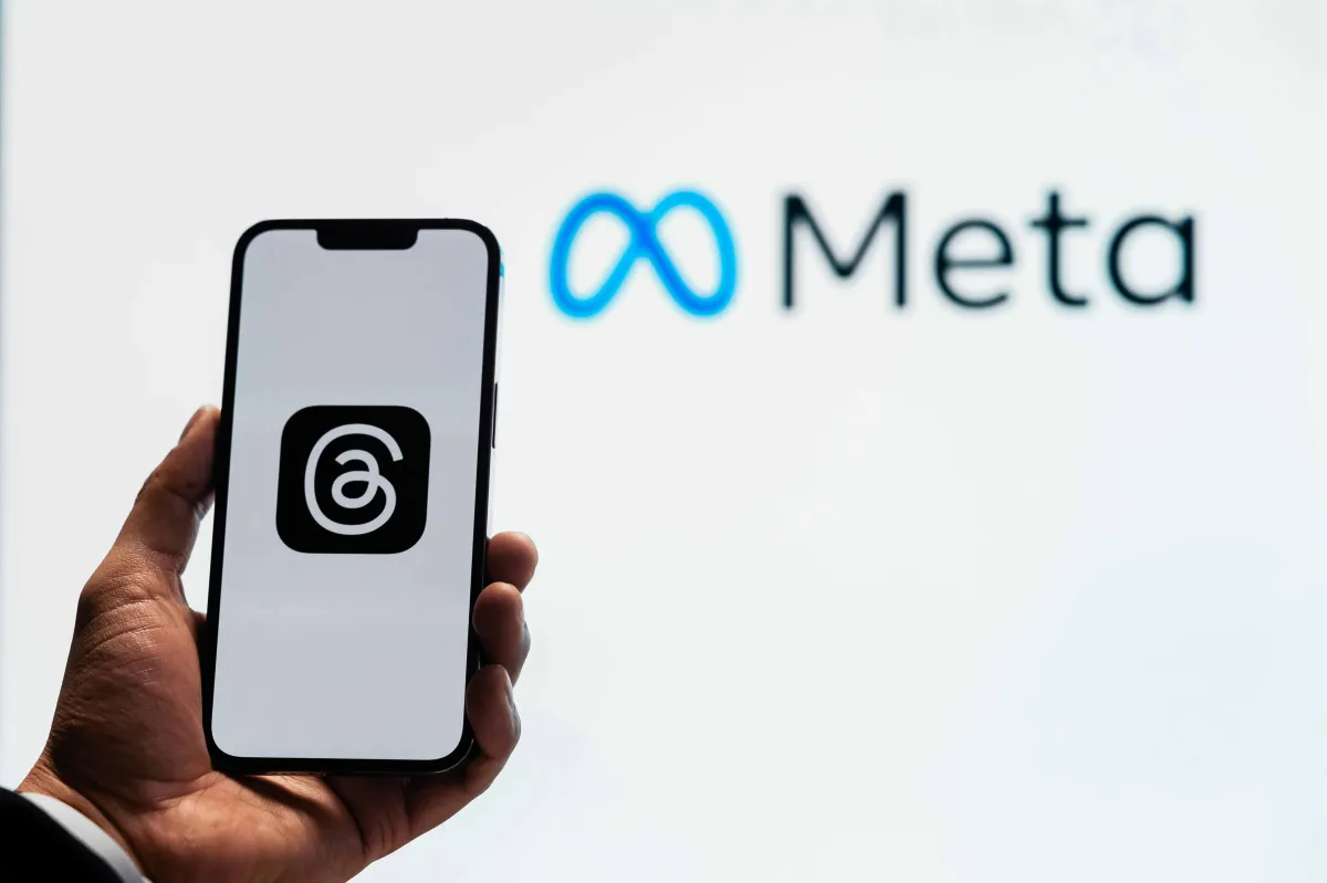 A hand holding a smartphone displaying the Threads app logo, with the Meta logo in the background, symbolizing advertising opportunities on Meta platforms