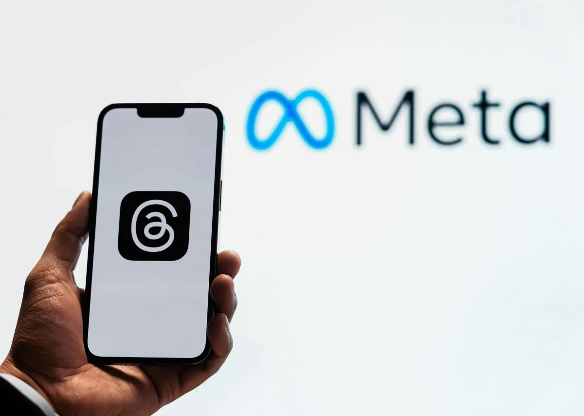 A hand holding a smartphone displaying the Threads app logo, with the Meta logo in the background, symbolizing advertising opportunities on Meta platforms