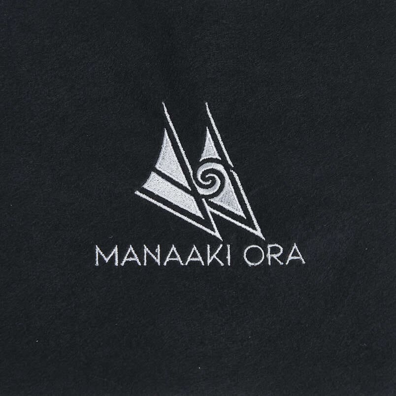 White Manaaki Ora logo embroidered on black fabric