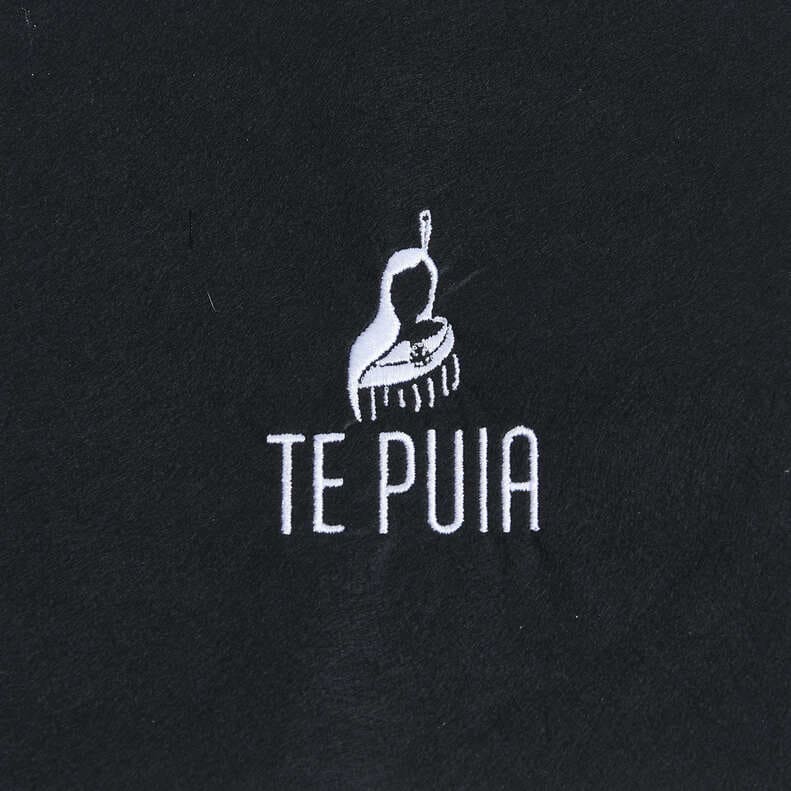 White Te Puia logo and cultural motif embroidered on black fabric