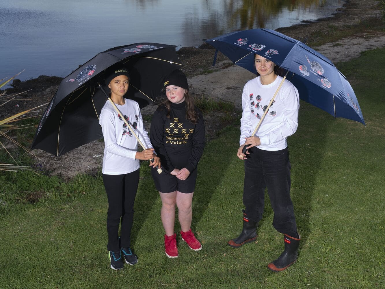 Three young people wearing Matariki-themed clothing with custom printed umbrellas