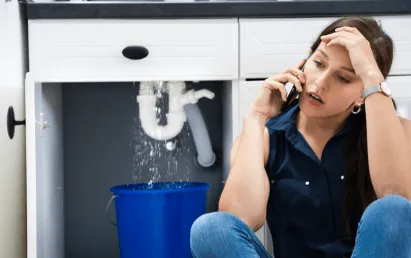 Woman on the phone has a plumbing emergency in San Antonio for a burst pipe under her sink