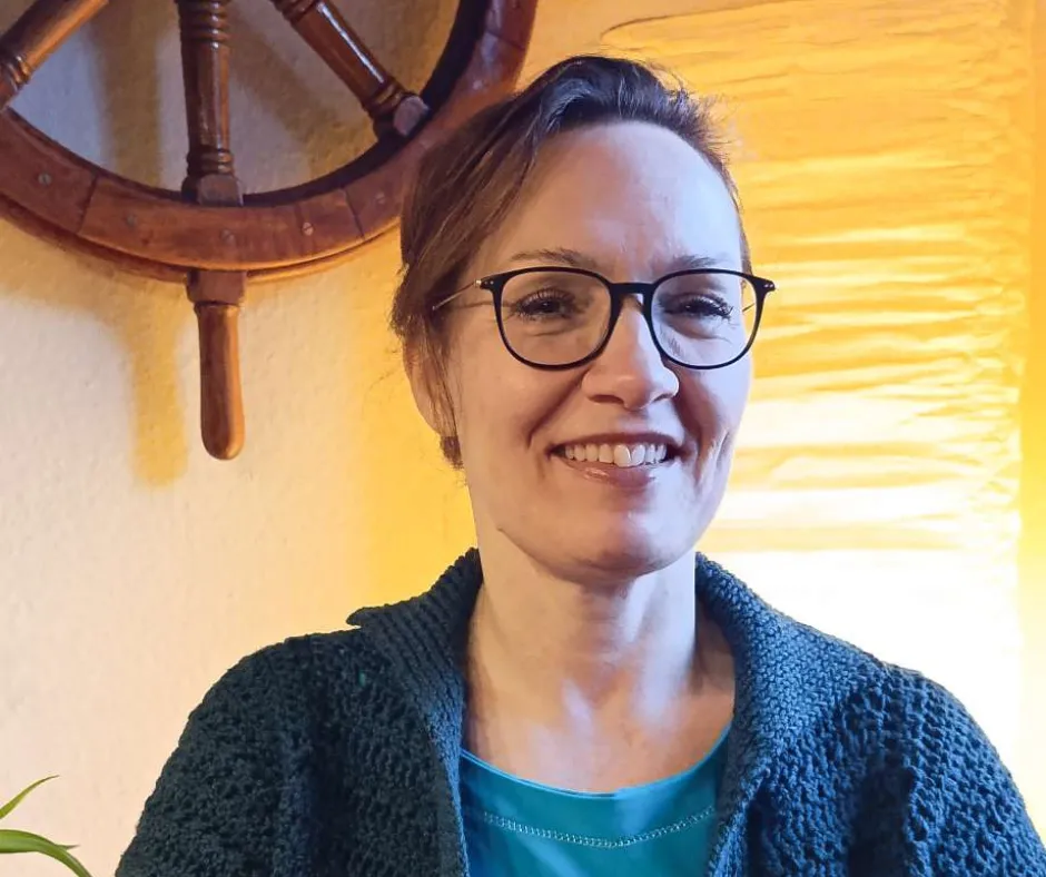 Katja mit Zwinkern, Hoptimist-Figur und Mini-Journal vor Sonnenuntergang an der Nordsee – Symbol für Leichtigkeit, Inspiration und kreativen Rückzug.