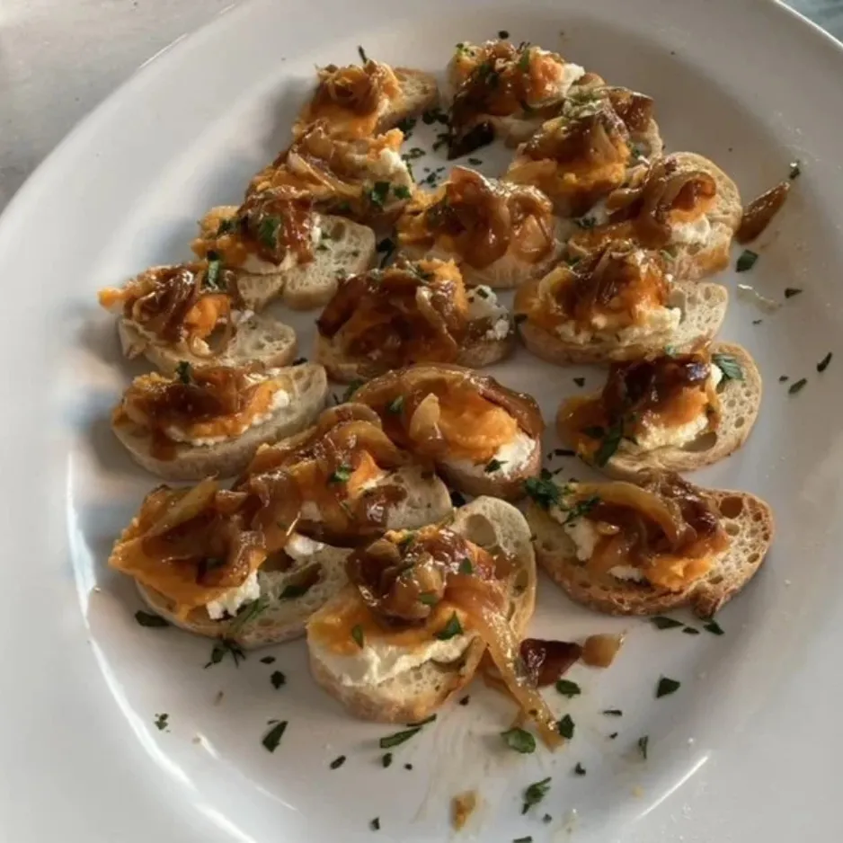 A white platter filled with elegant crostini appetizers topped with caramelized onions and goat cheese for a cocktail