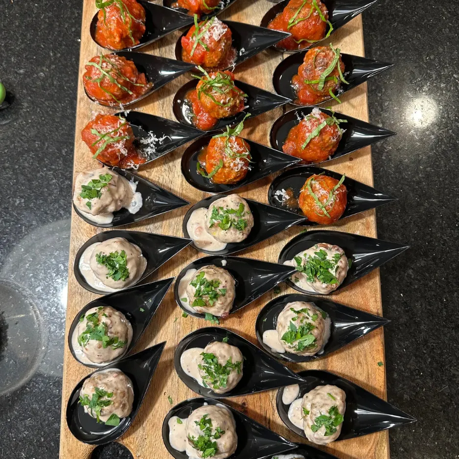 A beautiful arrangement of individual passed appetizers served on black tasting spoons for a luxury social gathering.