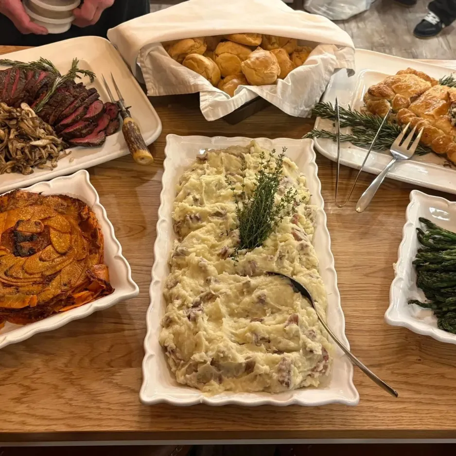 A hearty family-style dinner spread featuring garlic mashed potatoes, roasted asparagus, and sliced steak tenderloin.