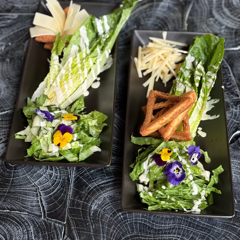 Two modernly styled Caesar salads garnished with edible flowers and artisan crackers for an upscale private gathering.