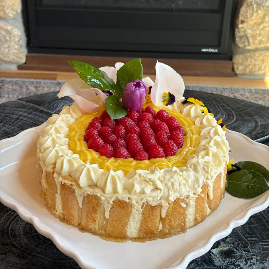 A stunning, custom-made dessert cake topped with fresh yellow mango and ripe red raspberries for a milestone birthday celebration.