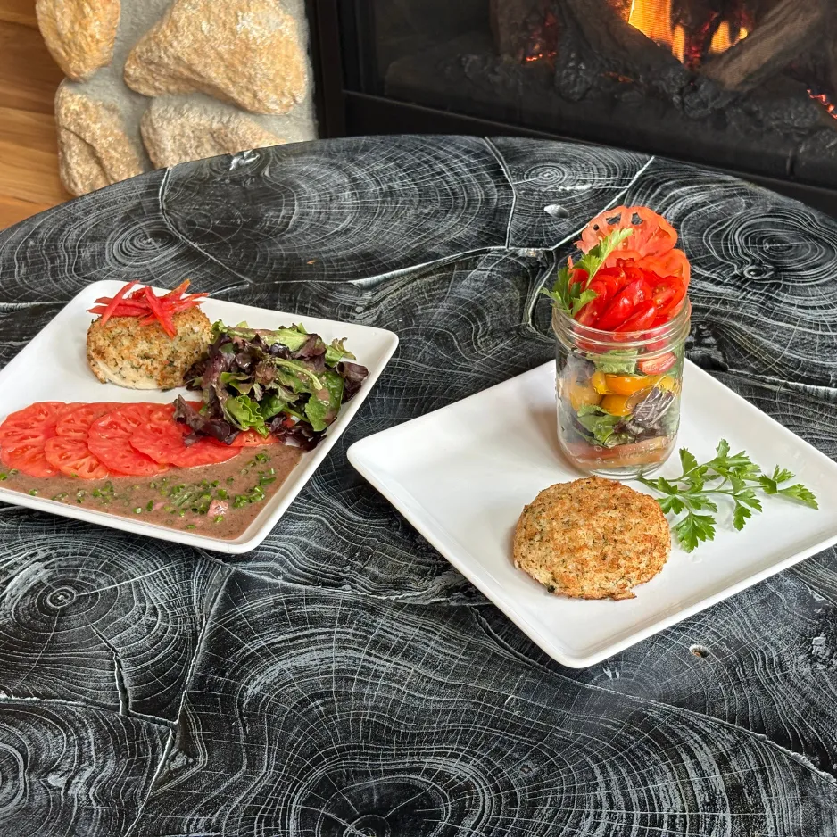 A cozy fireside dining experience featuring a multi-plated meal with fresh salads and savory crab cakes.