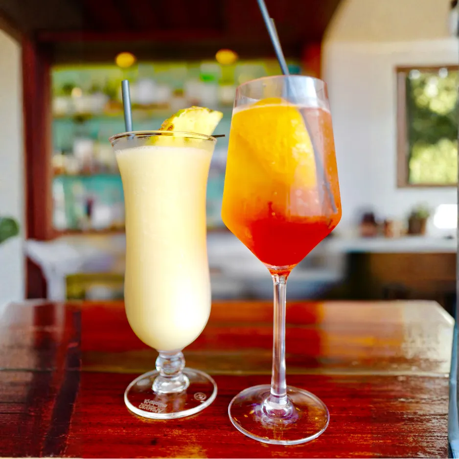 A tropical pineapple cocktail and a vibrant orange spritz served on a wooden table for a seasonal summer gathering.