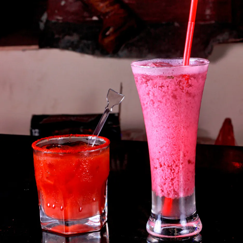 A frozen red margarita and a tall pink blended mocktail with straws, demonstrating diverse non-alcoholic and specialty drink options.