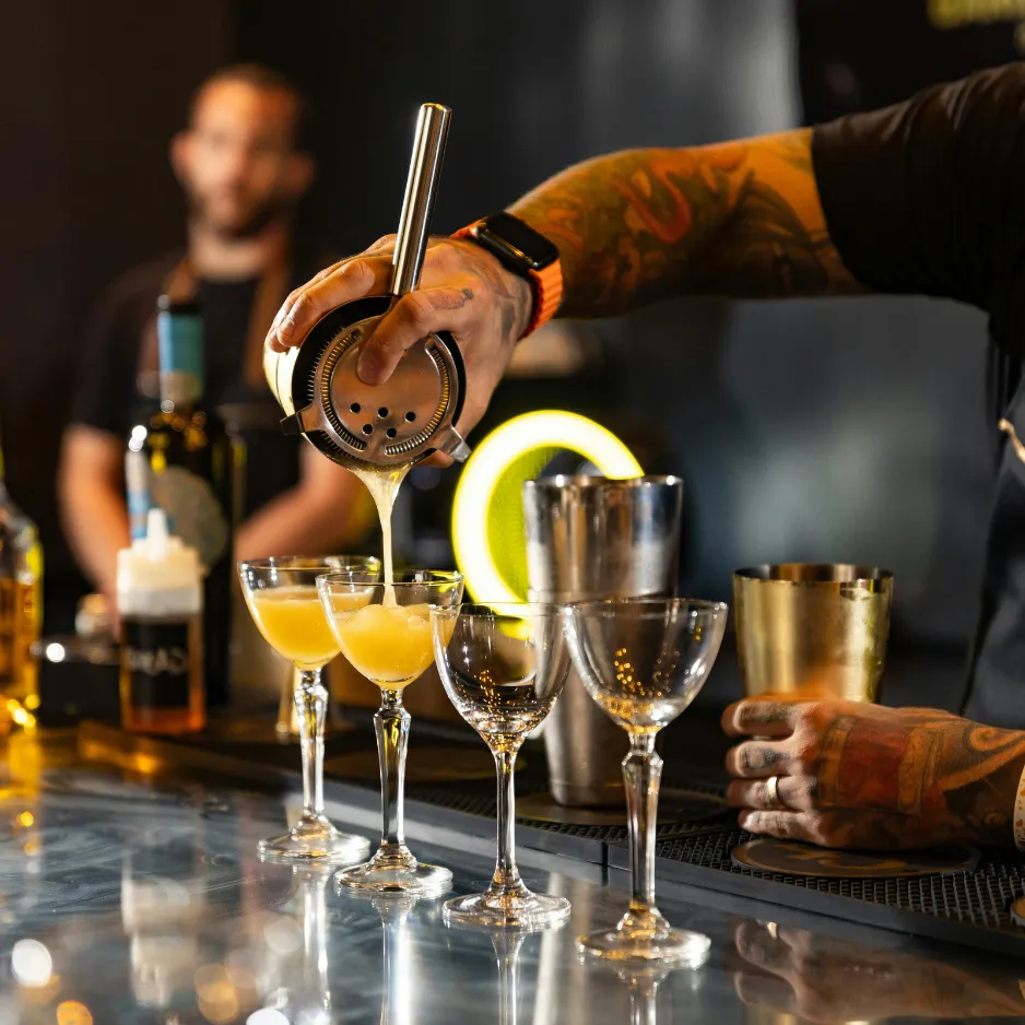 A professional event bartender carefully pouring a custom signature cocktail from a shaker during a corporate networking function.