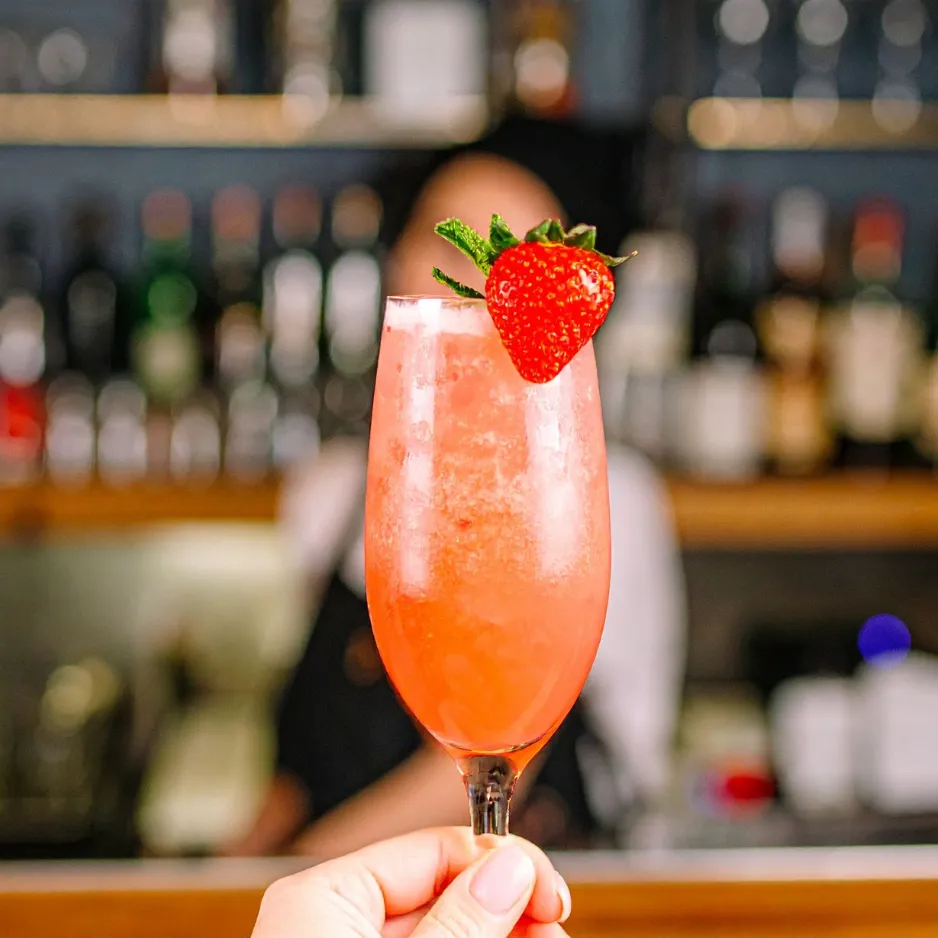 A crisp, bubbling champagne cocktail garnished with a fresh strawberry held up by an event bartender.