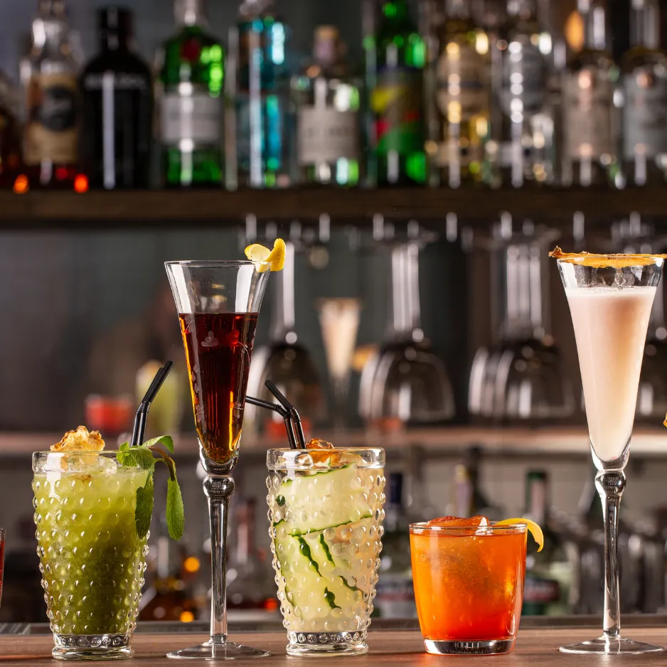 A diverse lineup of craft cocktails, including refreshing herb-infused highballs and elegant champagne flutes, at an event bar.