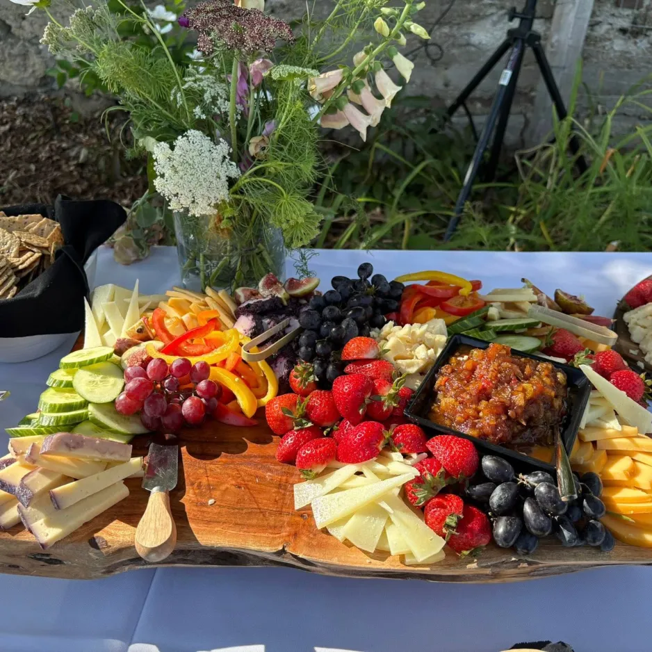 A large, rustic wooden charcuterie board loaded with fresh fruit, cheeses, and dips for a social cocktail hour.