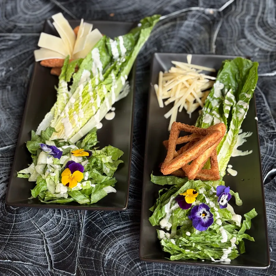 Two beautifully styled plates of romaine heart salads garnished with purple edible flowers for an upscale catered dinner.