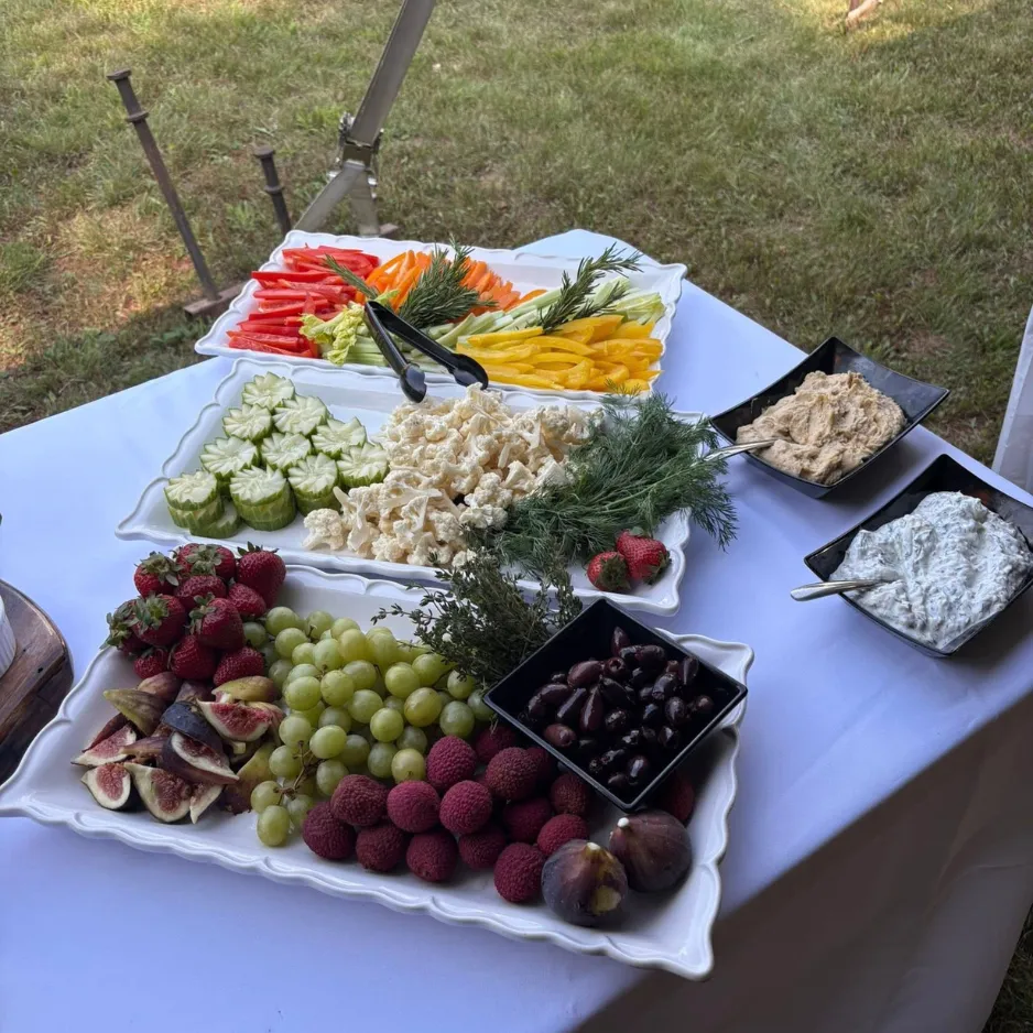 An outdoor food station featuring rows of fresh vegetable platters, fig and grape spreads, and dipping sauces.