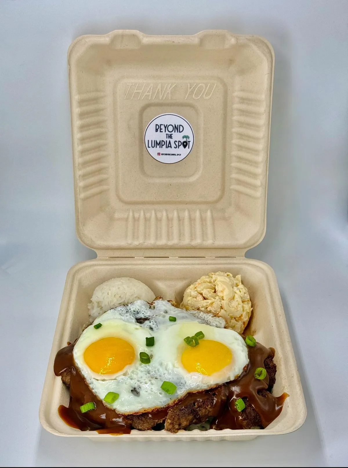 A close-up of golden Adobo Lumpia rolls arranged on a white plate, garnished with sliced green onions and a small bowl of calamansi dipping sauce, set on a light wooden table with a soft, airy background.