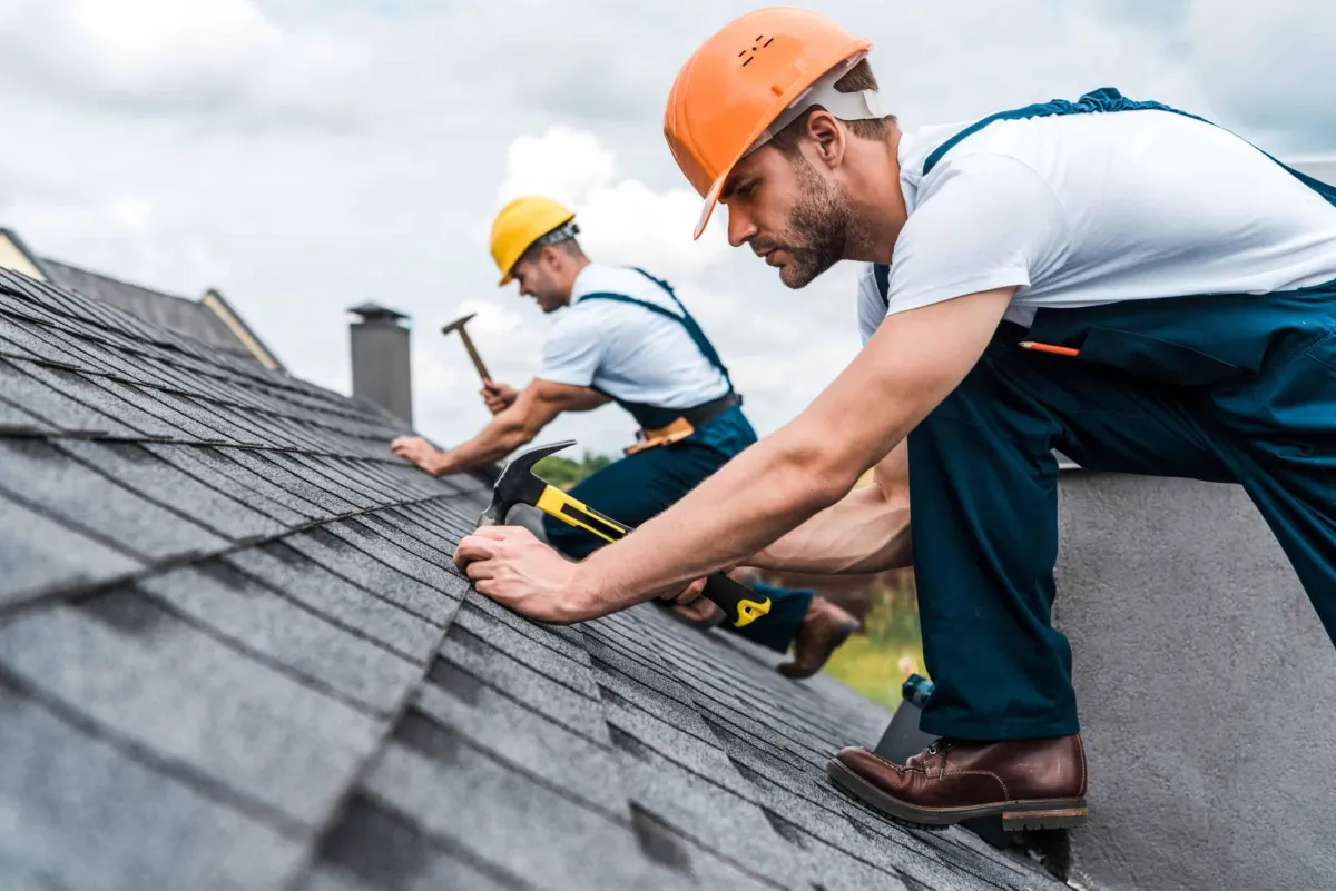 two men in work clothes installing shingles on a roof