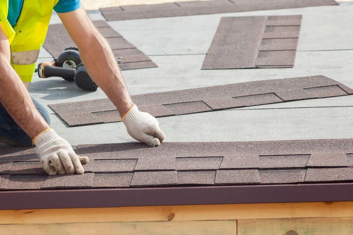 man with gloves installing asphalt shingles on roof deck