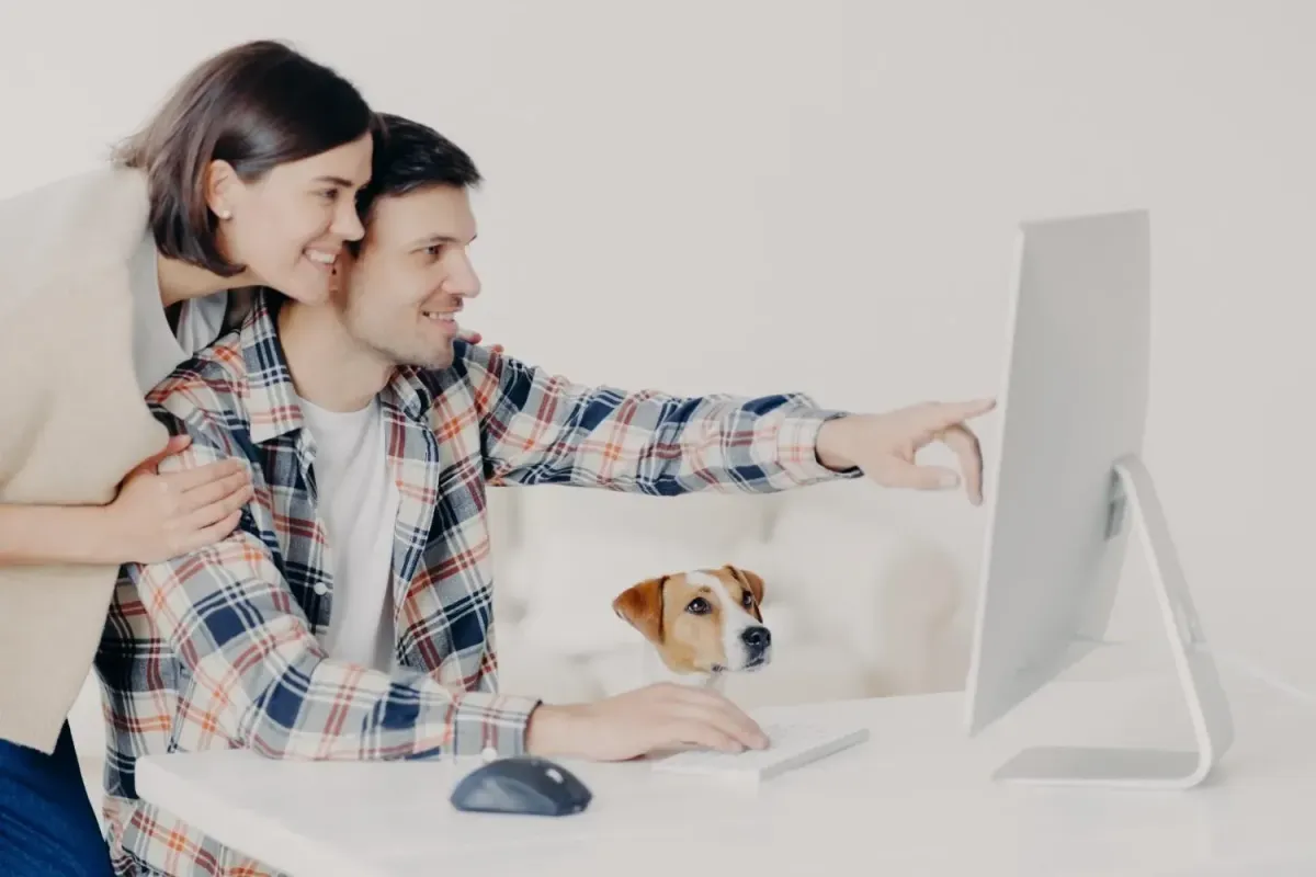 A diverse couple and their happy dog attentively viewing digital content on a laptop screen.