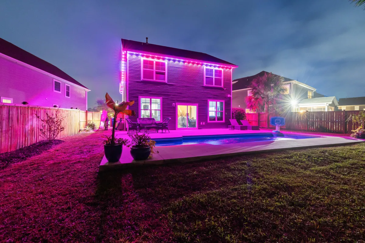 Backyard of a two-story house illuminated with purple and red EverBright permanent LED lights, perfect for celebrations.