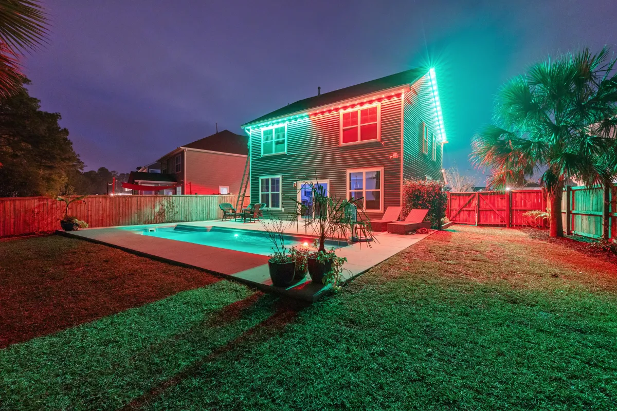 Backyard view of a home illuminated with EverBright Permanent Lights in vibrant red and green, highlighting the pool and landscaping for a festive atmosphere.