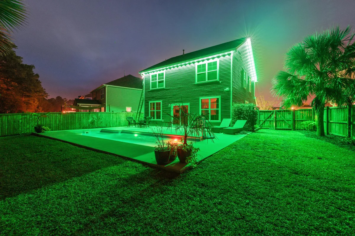 Backyard view of a two-story home lit with green EverBright permanent LED lights, creating a vibrant ambiance.