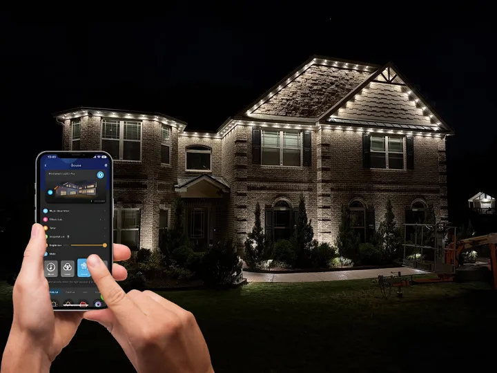 Hands controlling EverBright Permanent Lights with a smartphone app, showcasing a house lit up with vibrant, customizable colors for dynamic outdoor lighting.