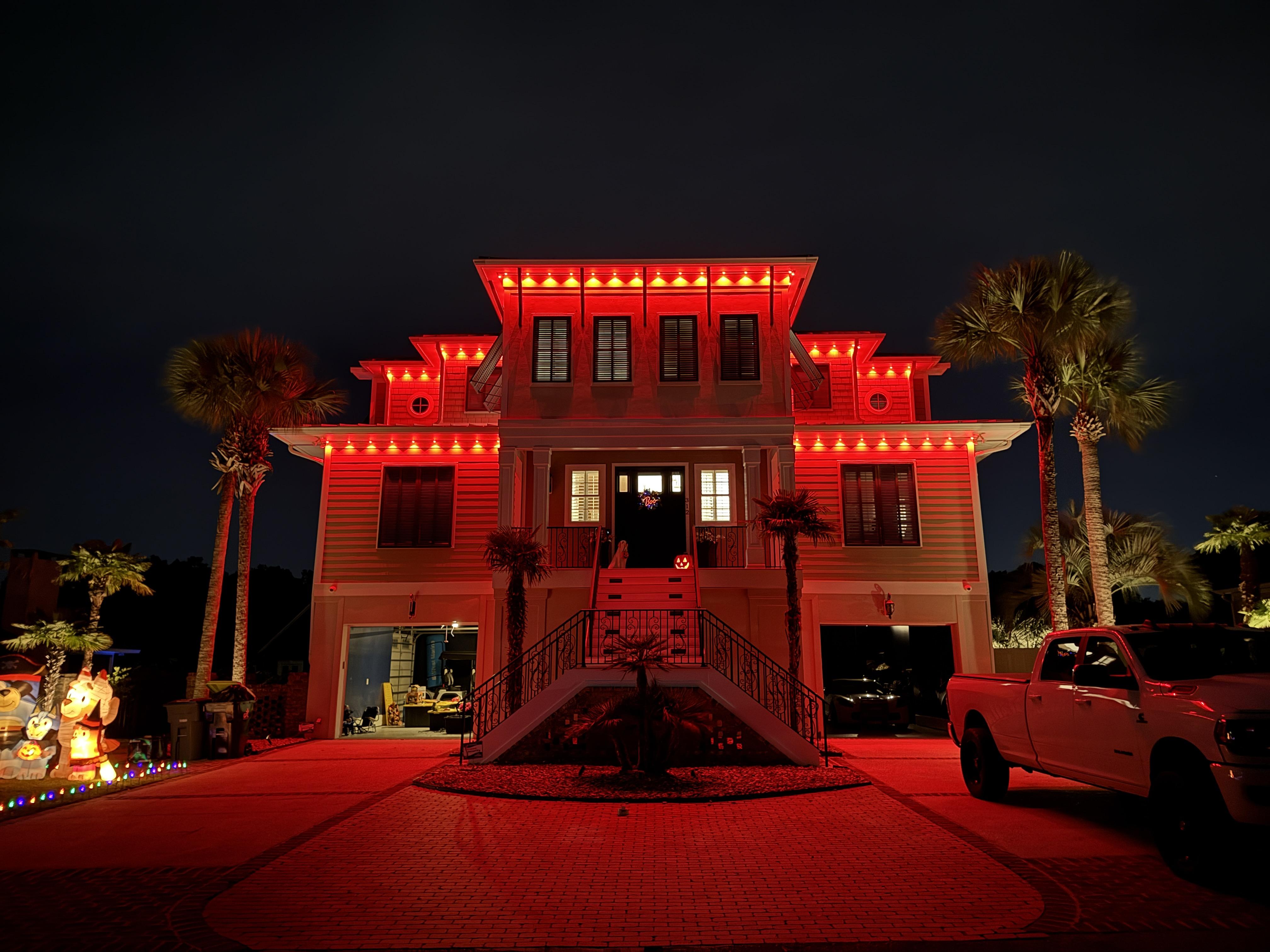 Backyard view of a home illuminated with EverBright Permanent Lights in vibrant red and green, highlighting the pool and landscaping for a festive atmosphere.