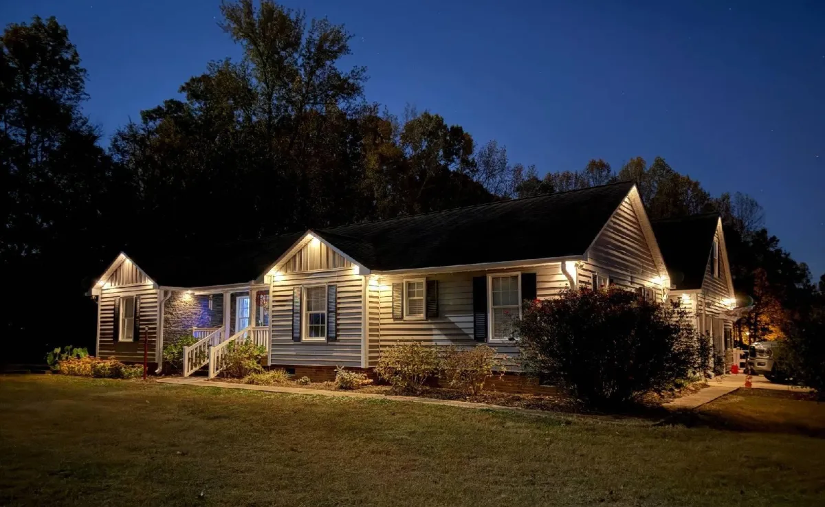 Two-story home illuminated with vibrant, customizable LED holiday lights controlled via a smartphone app shown in the foreground.