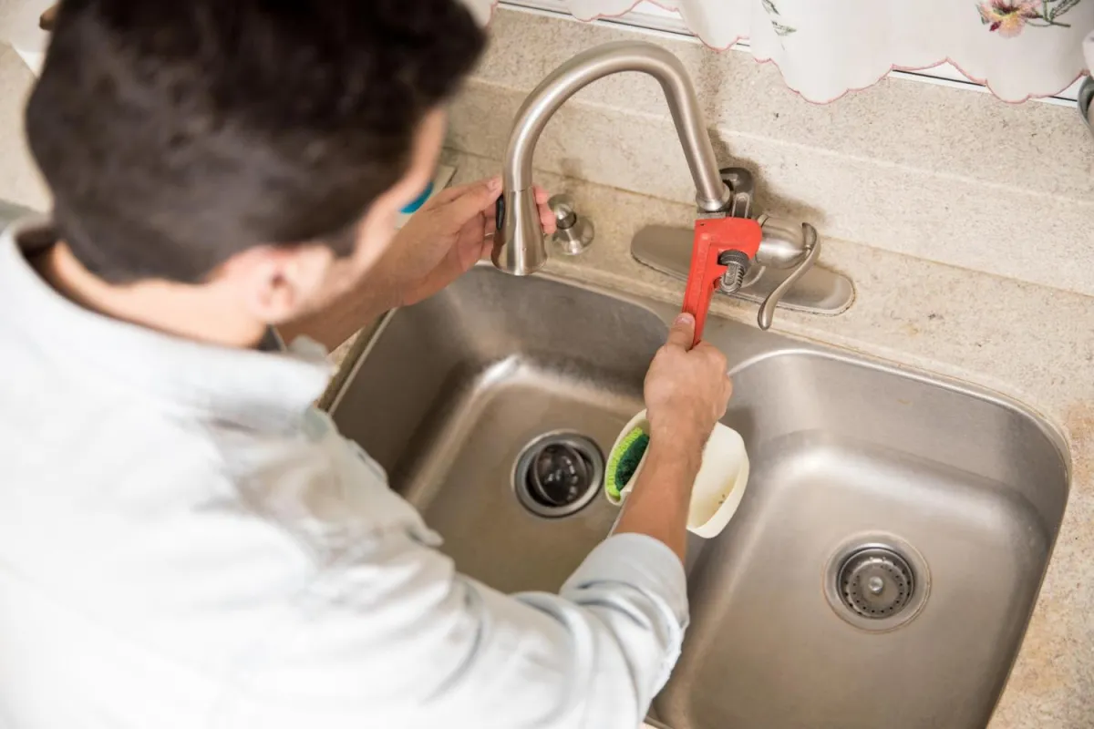 Plumber using a wrench to repair a kitchen sink faucet