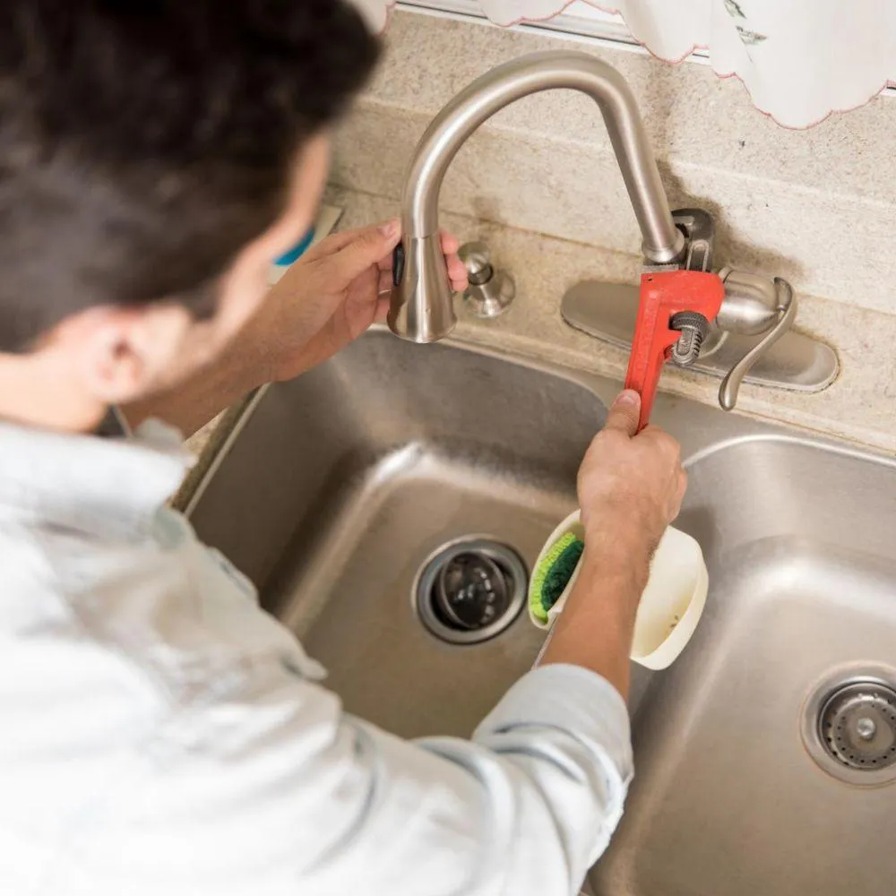 Plumber using a wrench to repair a kitchen sink faucet