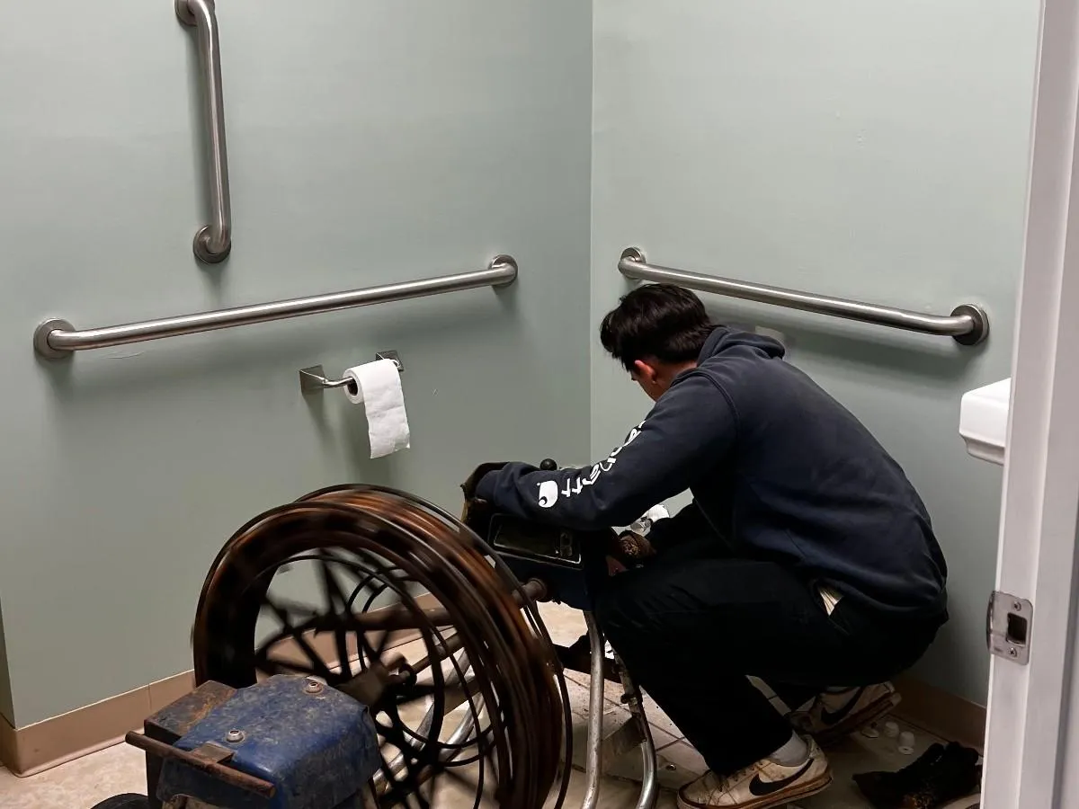 Elite Plumbing technician unclogging a commercial restroom drain with professional drain cleaning equipment