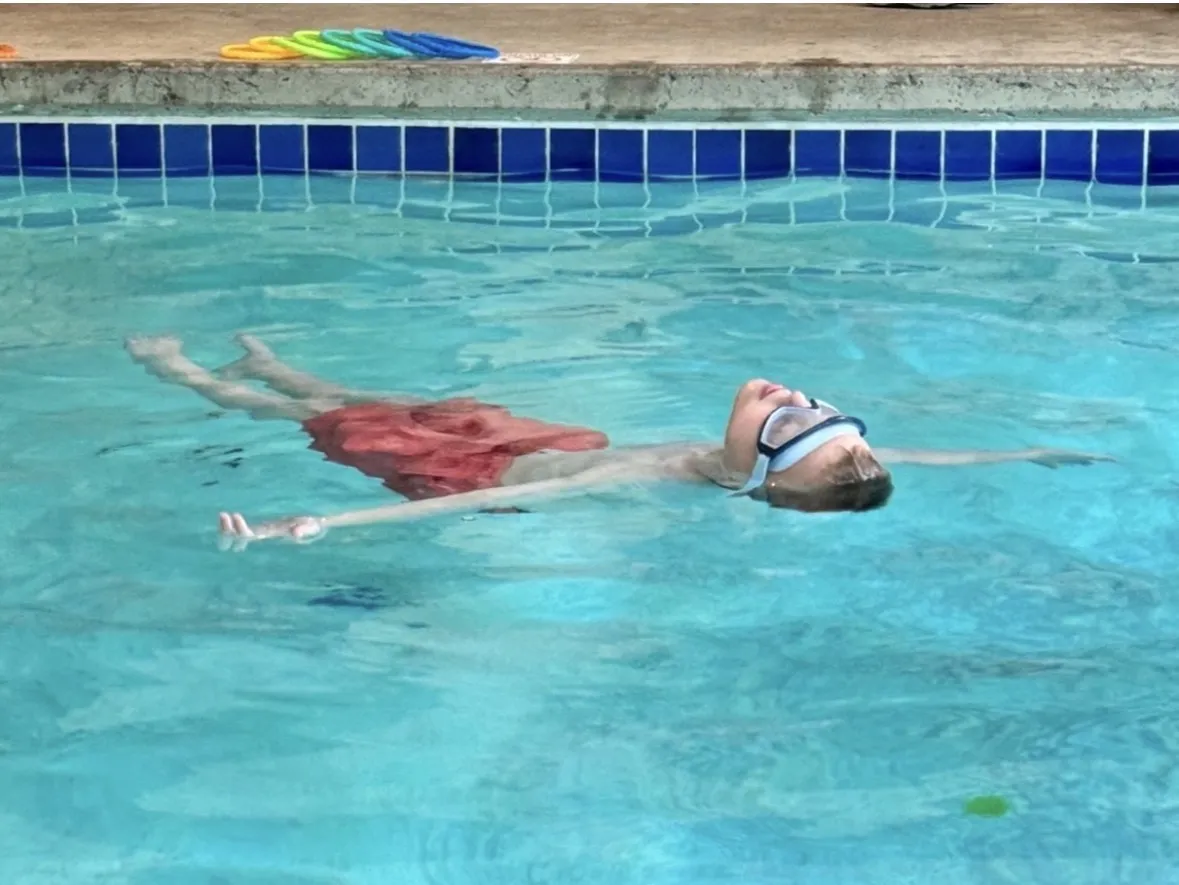 A young swimmer in goggles floating calmly on his back with arms spread wide