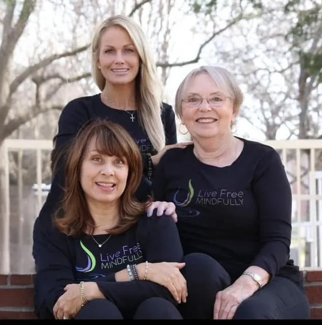 Portrait of a mid-40s non-binary facilitator with warm smile, neutral sweater, natural soft lighting against a light studio backdrop.