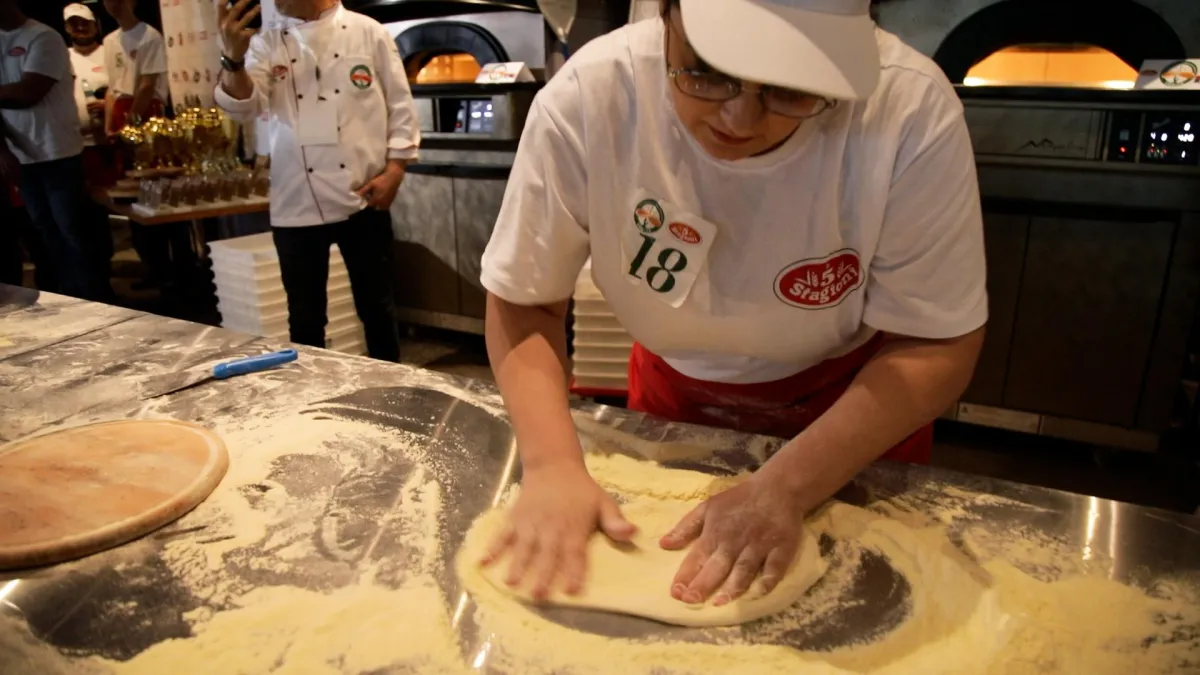 a man in an orange shirt making pizzas in a kitchen